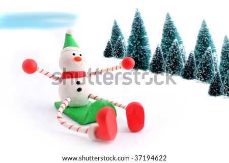 Snowman christmas character sliding down a snowhill on a sled with pine trees in the background, great for a greeting card (not isolated)