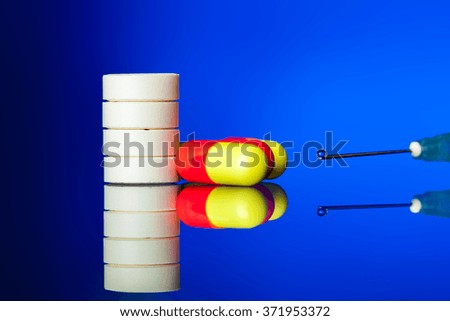 Tablets, pills and needle from a syringe with a vaccine drop on a blue background, nobody.