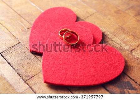 Two red felt hearts and wedding rings on wooden background closeup