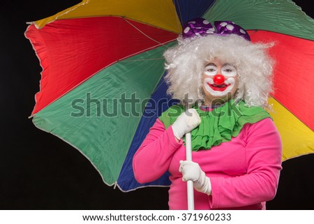 Jolly funny clown with a multi-colored umbrella on a black background