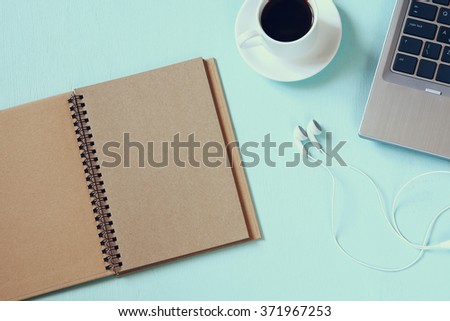 top view image of blank open notebook, cup of coffee and laptop over textured aqua background
