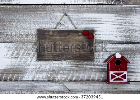 Blank wood sign with red heart hanging on antique rustic white wooden background with red barn birdhouse; family and love concept