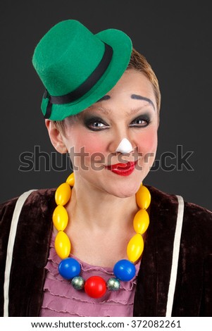 cheerful woman clown in a green hat on a gray background
