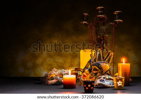 Classical venetian mask lying near lighting candle on dark background