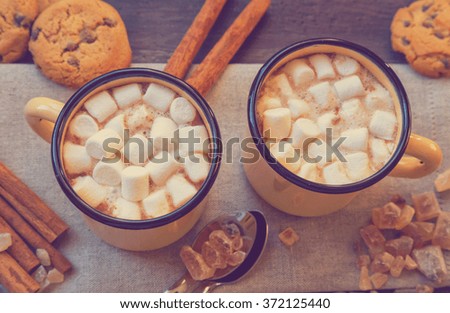 Two mugs filled with hot chocolate and marshmallows with cinnamon and brown sugar. Top view. Vintage toned picture.