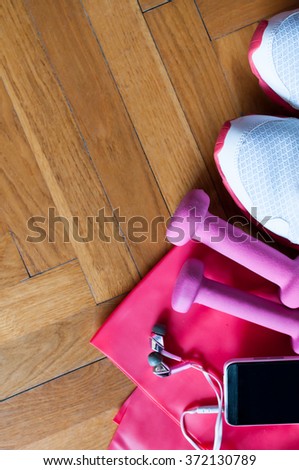 Sport equipment. Sneakers, dumbbells, smart phone with earphones and resistance band on wooden background.