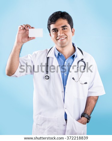 Handsome Indian Male Doctor showing or presenting empty white business card or blank board, standing isolated over blue background