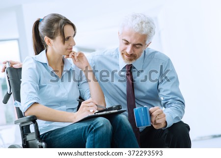 Businessman showing a document on a clipboard to a young woman in wheelchair, assistance and help concept