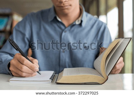 Business Man reading a book and writing notes on table.