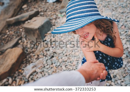 happy daughter in stripe hat holding mother hand on the beach. Family traveling on summer vacation. Cozy mood, candid shot.