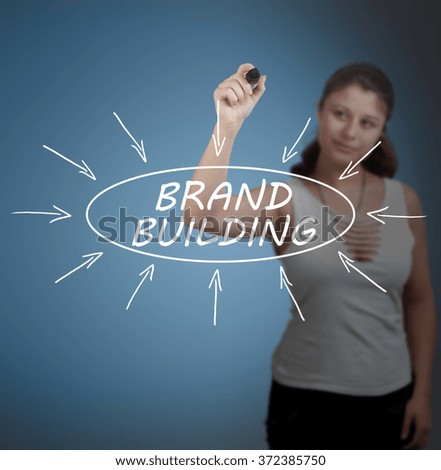 Brand Building - young businesswoman drawing information concept on transparent whiteboard in front of her.