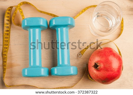 To bring the body into order. To go to fitness. Blue dumbbells, measuring tape, a pomegranate and a glass of water on wooden background
