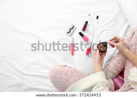 Woman in pajamas applying makeup on her bed