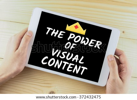 tablet in hand on wooden desk word the power of visual content