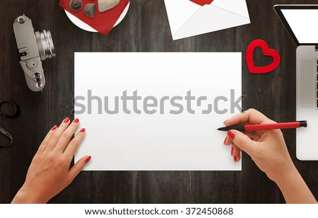 Woman hand writing on blank paper. Laptop, scissors, camera, sweets and envelope on wooden table.