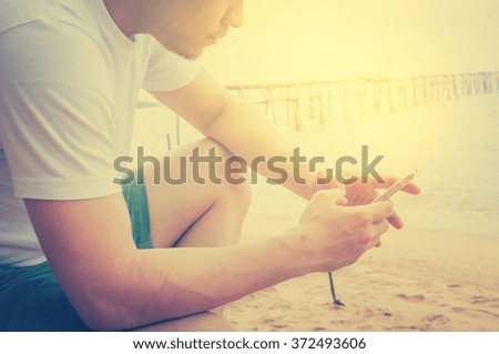 Young and traveler man sitting beside the sea and playing on his mobile phone
