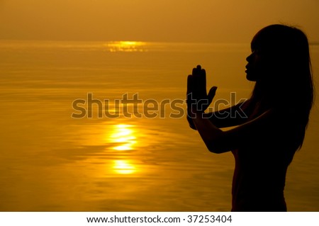 Prayer. Woman with hands folded at seaside during sunset.