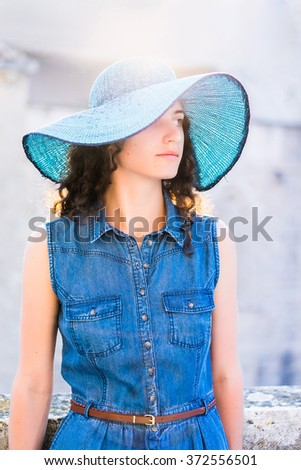 Pretty brunette girl in wide brim blue hat with a camera walking in the old town at sunset.