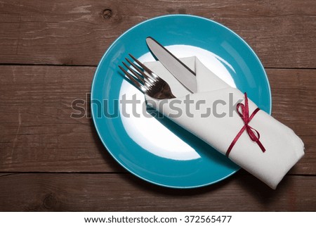 Plate, fork and knife in napkin on wooden background. Toned.