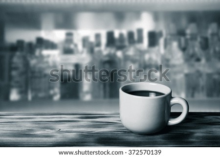 Coffee in cup on wooden table opposite a blurred background. Toned.