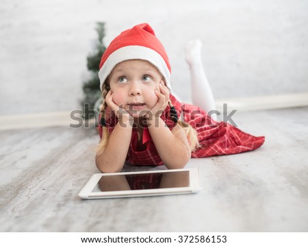 Little girl in hat of Santa Claus with digital tablet