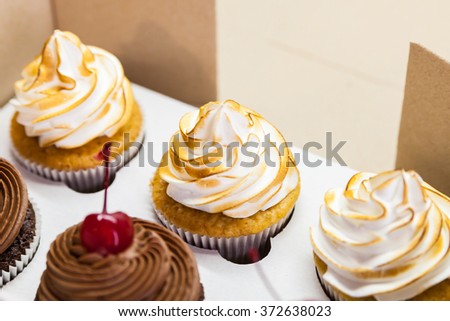 Box with lemon cupcakes with meringue and chocolate cupcakes with cherries