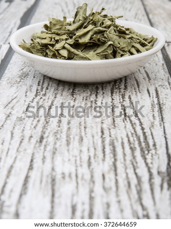 Dried curry leaves in white bowl over wooden background