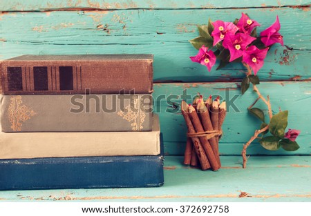 stack of old books next to colorful pencils and bougainvillea flower on wooden table. vintage filtered image
