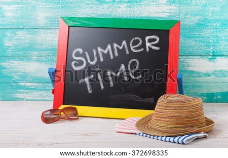 Blackboard with text it's summer time. Summer accessories sunglasses, hat, towel on wooden deck