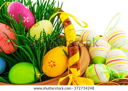 Macro view of wicker wooden basket with Easter eggs, fresh grass and color ribbons on white background