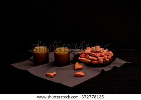 A plate of cookies with red heart-shaped, two mugs of coffee with milk, Valentine's Day, black background, side view, copy space
