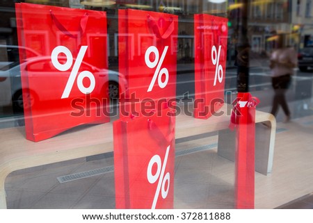Window display with sale. Big red shopping bags with sign of percent on the storefront. Reflections of the city street on the shop-window
