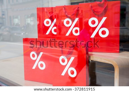 Window display with sale. Big red shopping bags with sign of percent on the storefront. Reflections of the city street on the shop-window