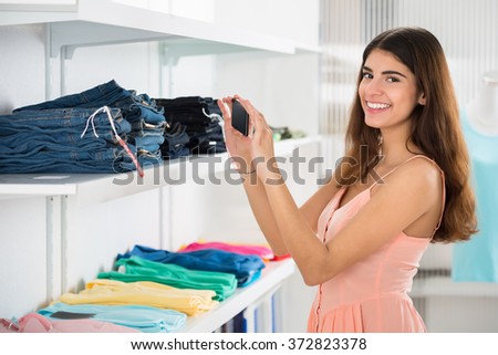 Portrait of happy young woman photographing garments through smartphone in retail store