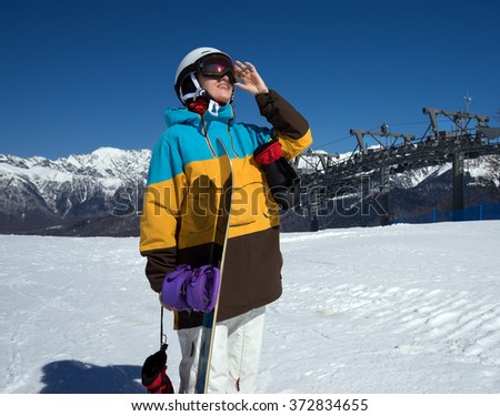 Portrait of woman snowboarder on background beautiful landscape of snowy high mountains of Caucasus at Krasnaya Polyana, standing with snowboard
