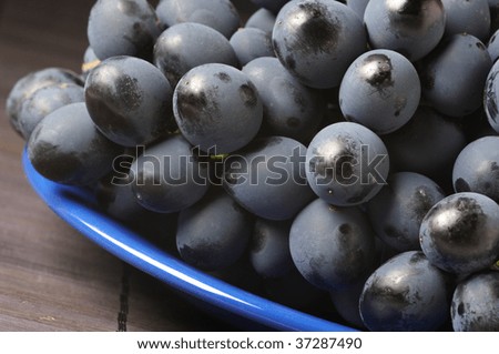 Bunch of fresh ripe dark grape with bloom on blue plate.