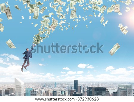 young businessman flying over Paris with a magnet in hand that is pulled to money tornado. Paris and blue sky at the background. Concept of strivig for wealth.
