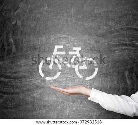 hand as if holding a bicycle drawn on the blackboard. Concept of eco traveling. Royalty-Free Stock Photo #372932518