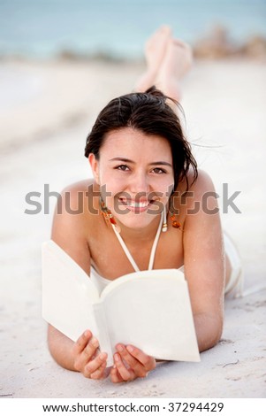 Beautiful woman lying on the beach with a book