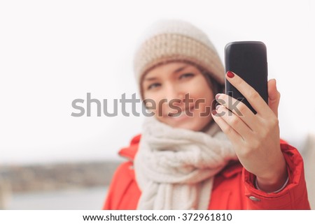 Young woman using  mobile cell phone in winter or fall. Cheerful happy young woman in red jacket smiling outdoors sending message.