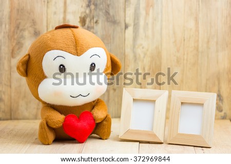 Happy smiling monkey doll hugging red heart with two picture frame sitting on wood, gift of love concept