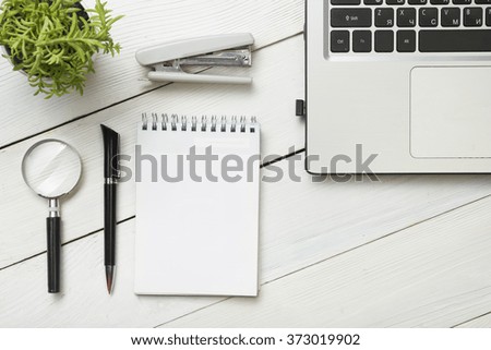 Office desk table with supplies. Top view. Copy space for text. Laptop, blank notepad, pen, magnifying glass, calculator, reminder, flower.