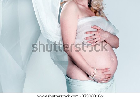 Pregnant woman wrapped in veil on blue background.