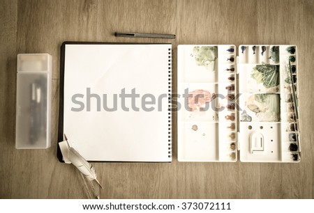 Top view of notebook and artist color palette on wood floor vintage picture style