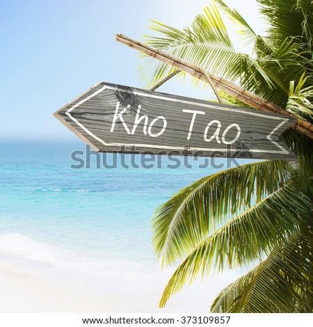 Wooden sign Kho Tao on tropical white sand beach summer background. Lush tropical foliage and sunshine. Blue ocean at perfect day. No people.