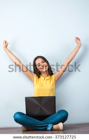 Photo of beautiful young business woman sitting on wooden floor. Smiling woman with yellow shirt and laptop stretching