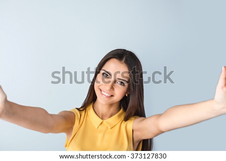 Photo of beautiful young business woman standing near gray background. Woman with yellow shirt making selfie, looking at camera and smiling