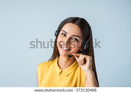 Photo of beautiful young call center operator standing near gray background. Woman with headphones looking at camera and smiling Royalty-Free Stock Photo #373130488