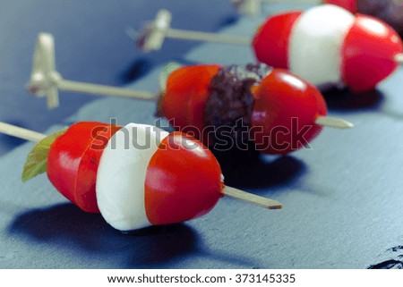 Small snacks canape with cherry tomatoes, mozzarella and meatbolls on skewer on a black slate plate. Shallow depth of field. Toned.