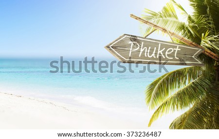 Wooden sign Phuket on tropical white sand beach summer background. Lush tropical foliage and sunshine. Blue ocean at perfect day. No people.
